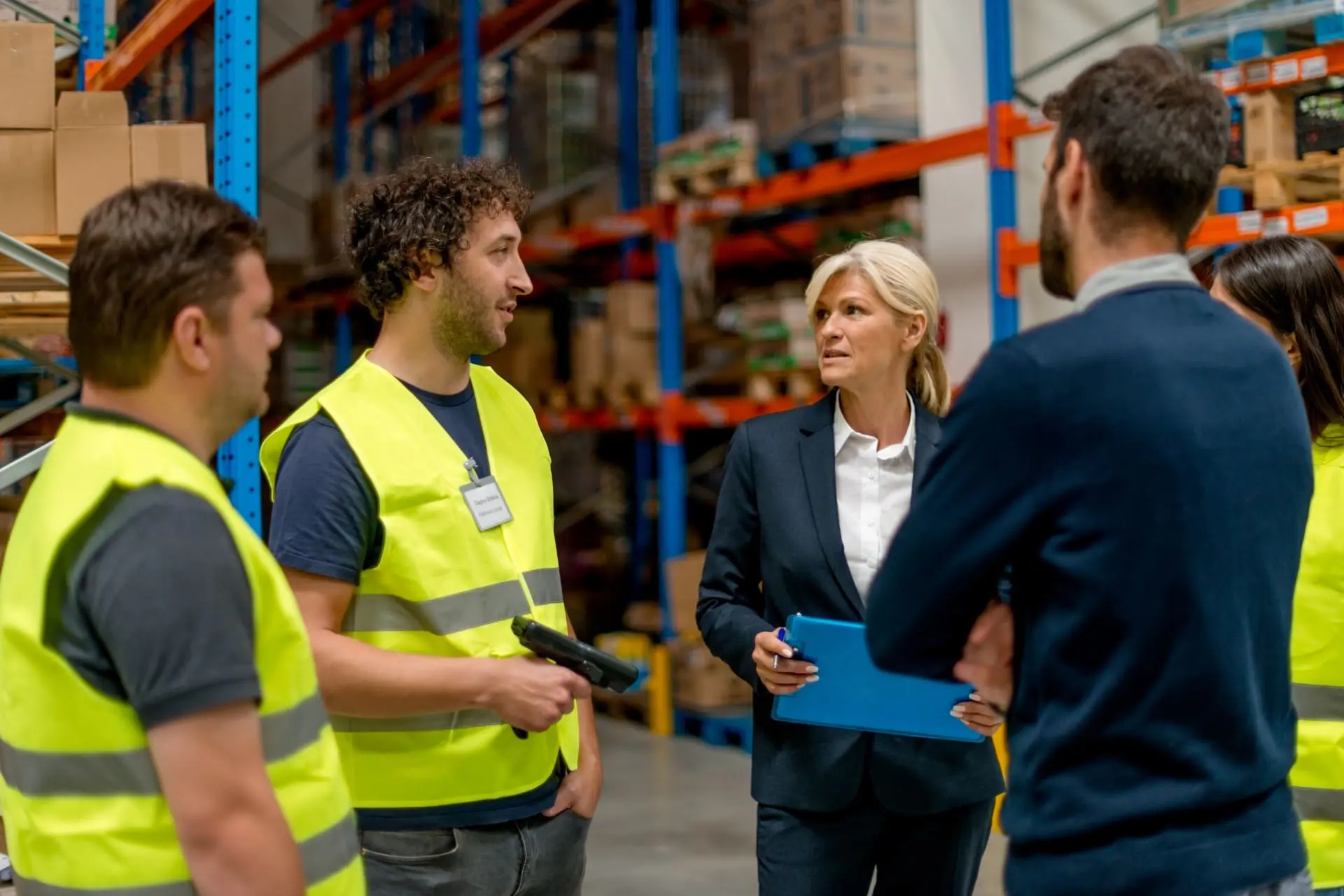 team in warehouse with woman in suit leading the conversation