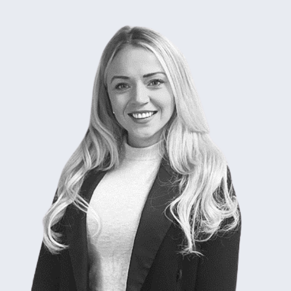 Black and white image of a woman with long blonde hair, wearing a white top and a black business jacket, smiling at the camera. 