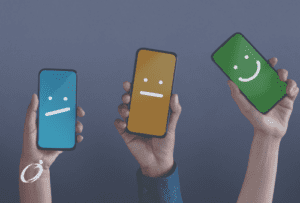 Photo showing 3 hands holding up smartphones. Each smartphone has a different background colour and facial expression (eyes and mouth) drawn on the screens, ranging from unhappy to happy.